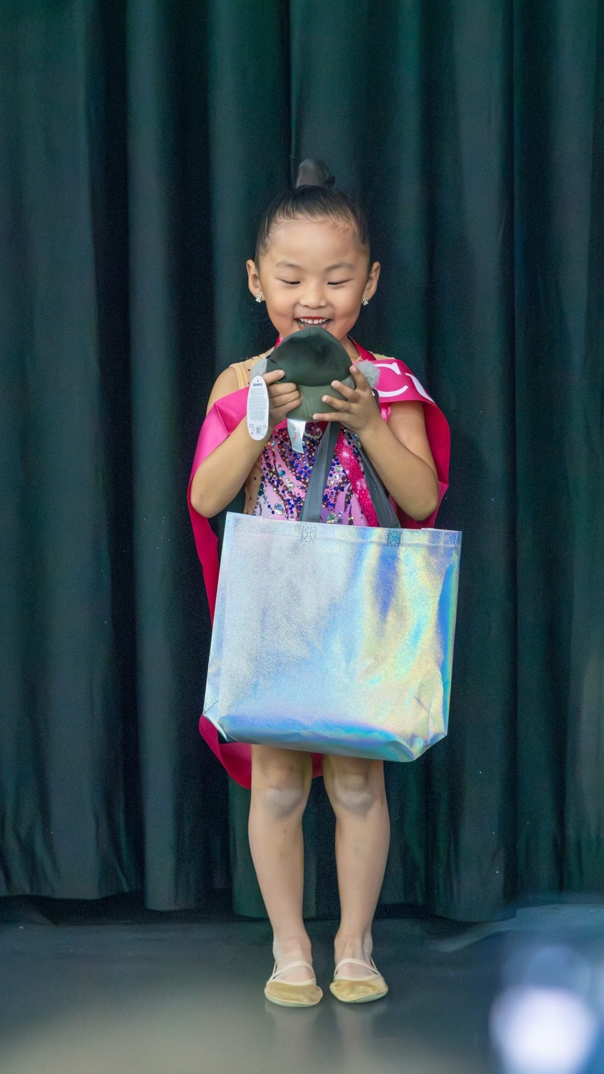 Smiling young gymnast on stage holding a gift bag