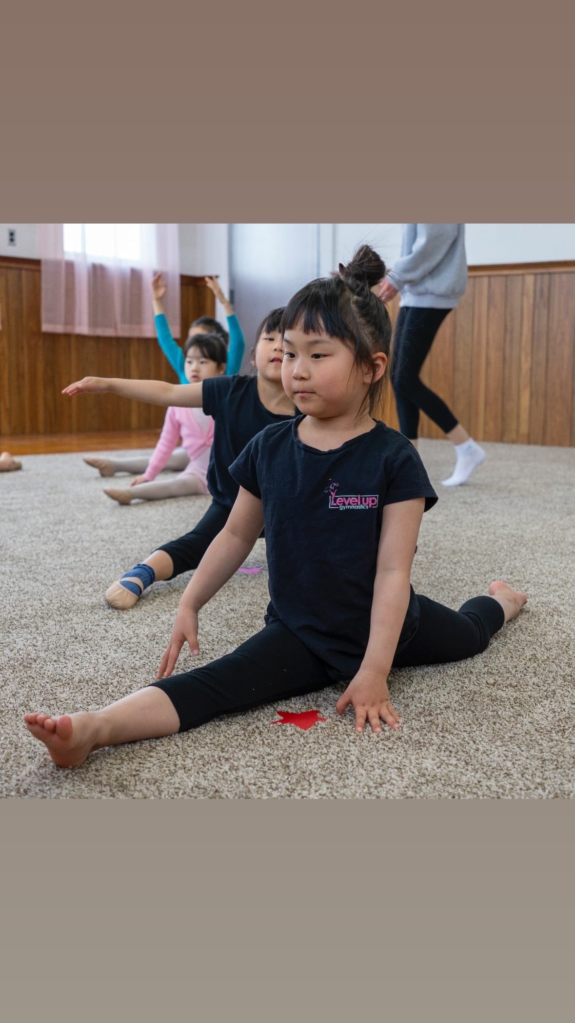 Young gymnast in a Level Up shirt practicing a split
