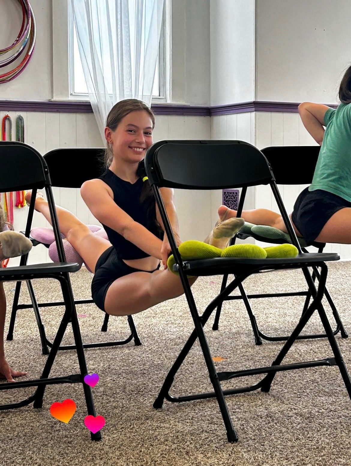 Gymnast smiling while stretching in a split between two chairs