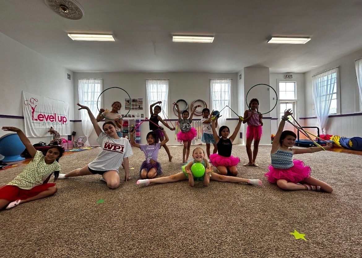Level Up campers posing with hoops, ribbons and a ball in the gym